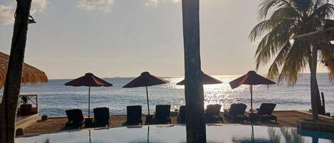 Vista de la piscina con sillas de descanso y sombrillas, con vista al mar.