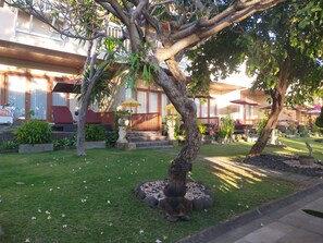 A courtyard with a tree, outdoor seating, and a building with a balcony. - Tauch Terminal Resort Tulamben & Spa (Rendang)