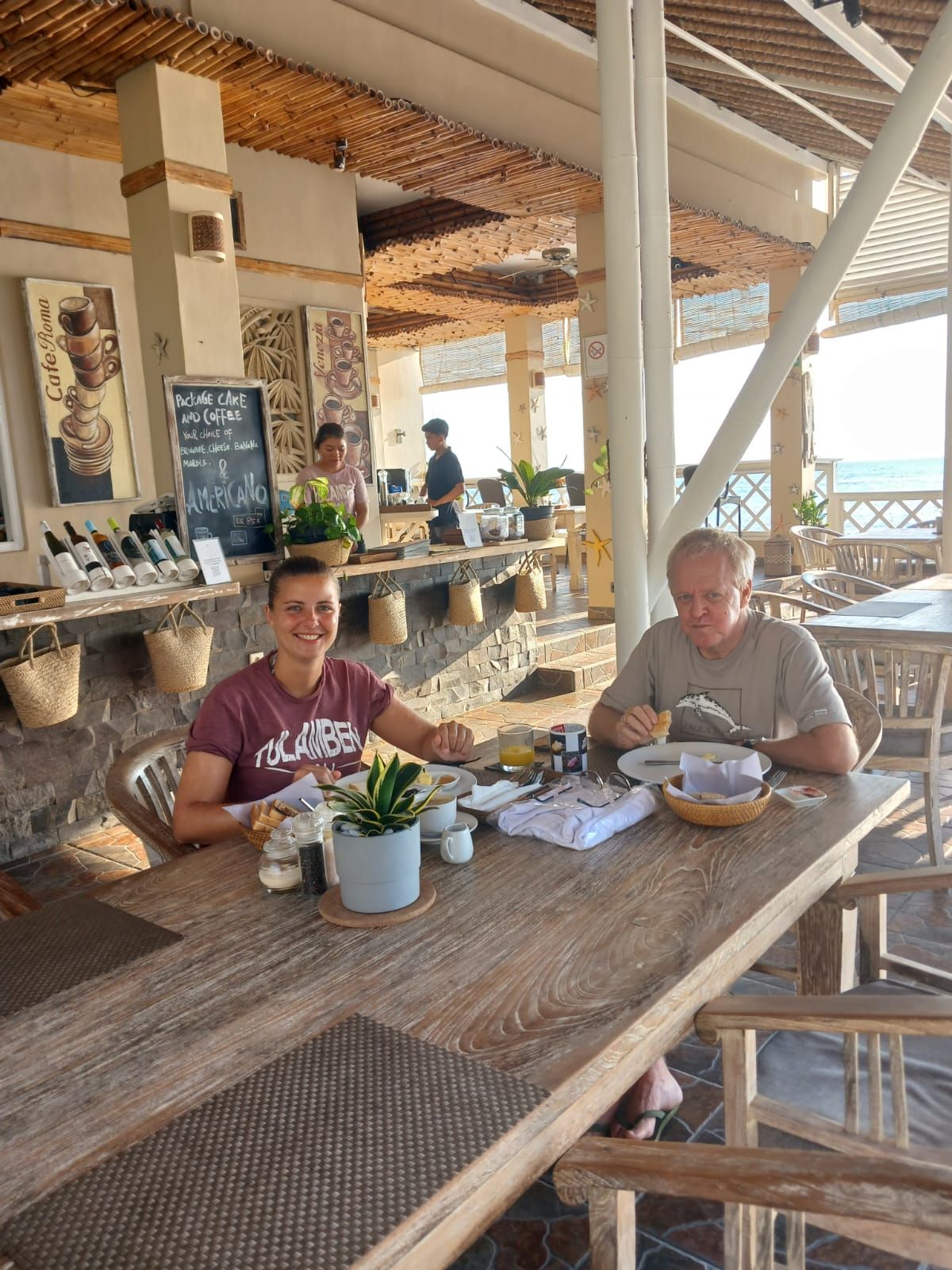 A restaurant with outdoor seating, a stone wall, and a view of the sea.