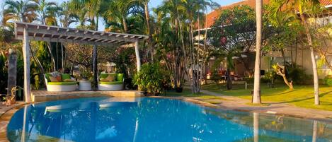 A swimming pool with a pergola, palm trees, and a building with a red roof.