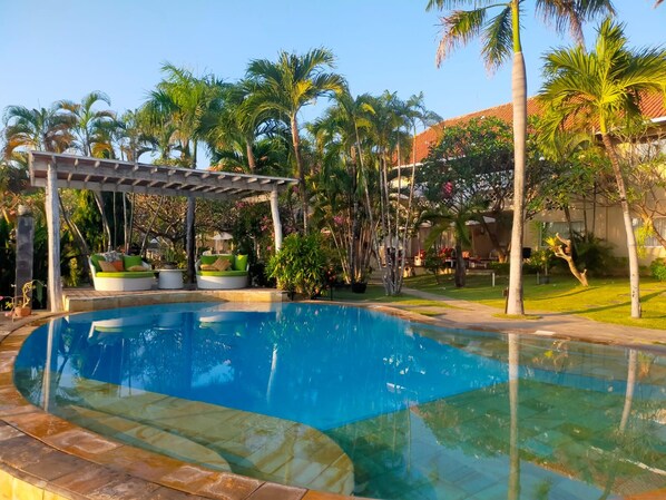 A swimming pool with a pergola, palm trees, and a building with a red roof.