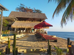 A beachfront resort with a thatched-roof building, outdoor seating, and a pool.