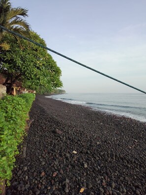 A beach with black pebbles, a rope, and green foliage.