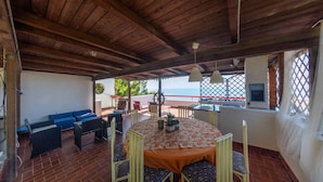 A covered patio with a table and chairs, a blue sofa, and a view of the sea. - Beautiful home in Sperlonga (Sperlonga)