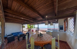A covered patio with a table and chairs, a blue sofa, and a view of the sea. - Beautiful home in Sperlonga (Sperlonga)