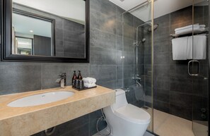 A modern bathroom with a large mirror, a sink, a toilet, and a glass-enclosed shower. - Alcove Da Nang Bay Boutique Hotel (Da Nang Municipality)