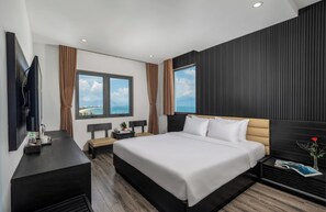 A modern hotel room with a large bed, a flat-screen TV, a bedside table with a lamp, and a view of the sea through large windows. - Alcove Da Nang Bay Boutique Hotel (Da Nang Municipality)