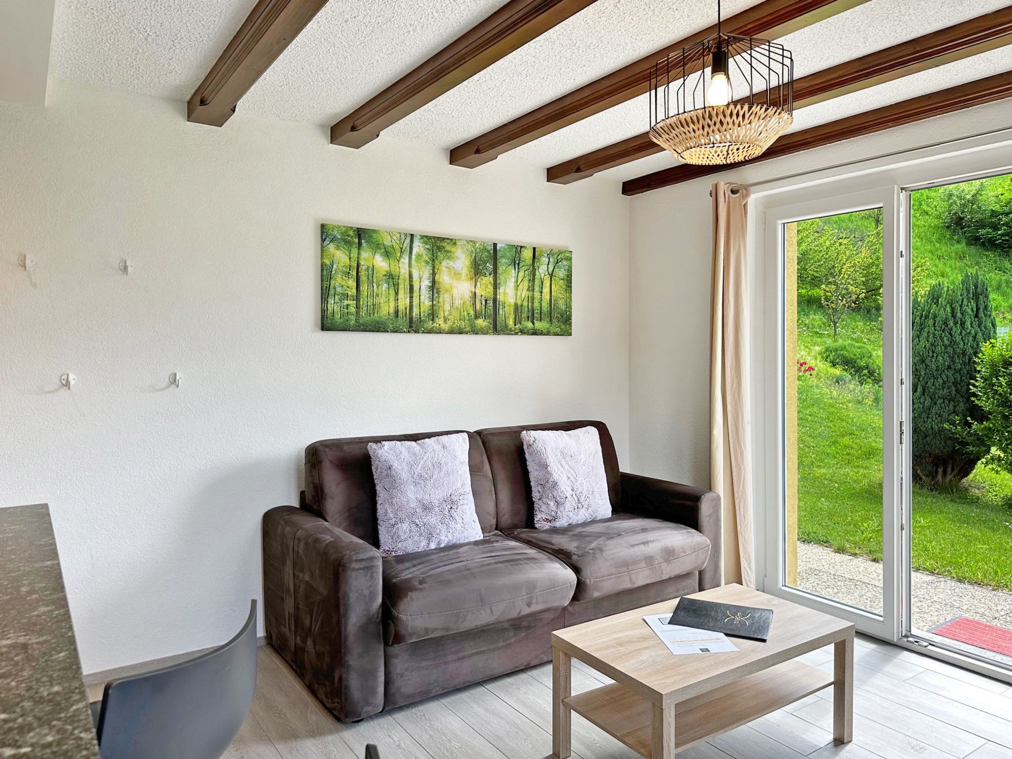 Un salon moderne avec un canapé, une table basse et une grande fenêtre donnant sur un paysage verdoyant.