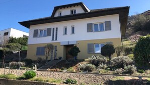Una casa de dos pisos con techo plano, una entrada principal y un pequeño jardín delantero con arbustos y un árbol.