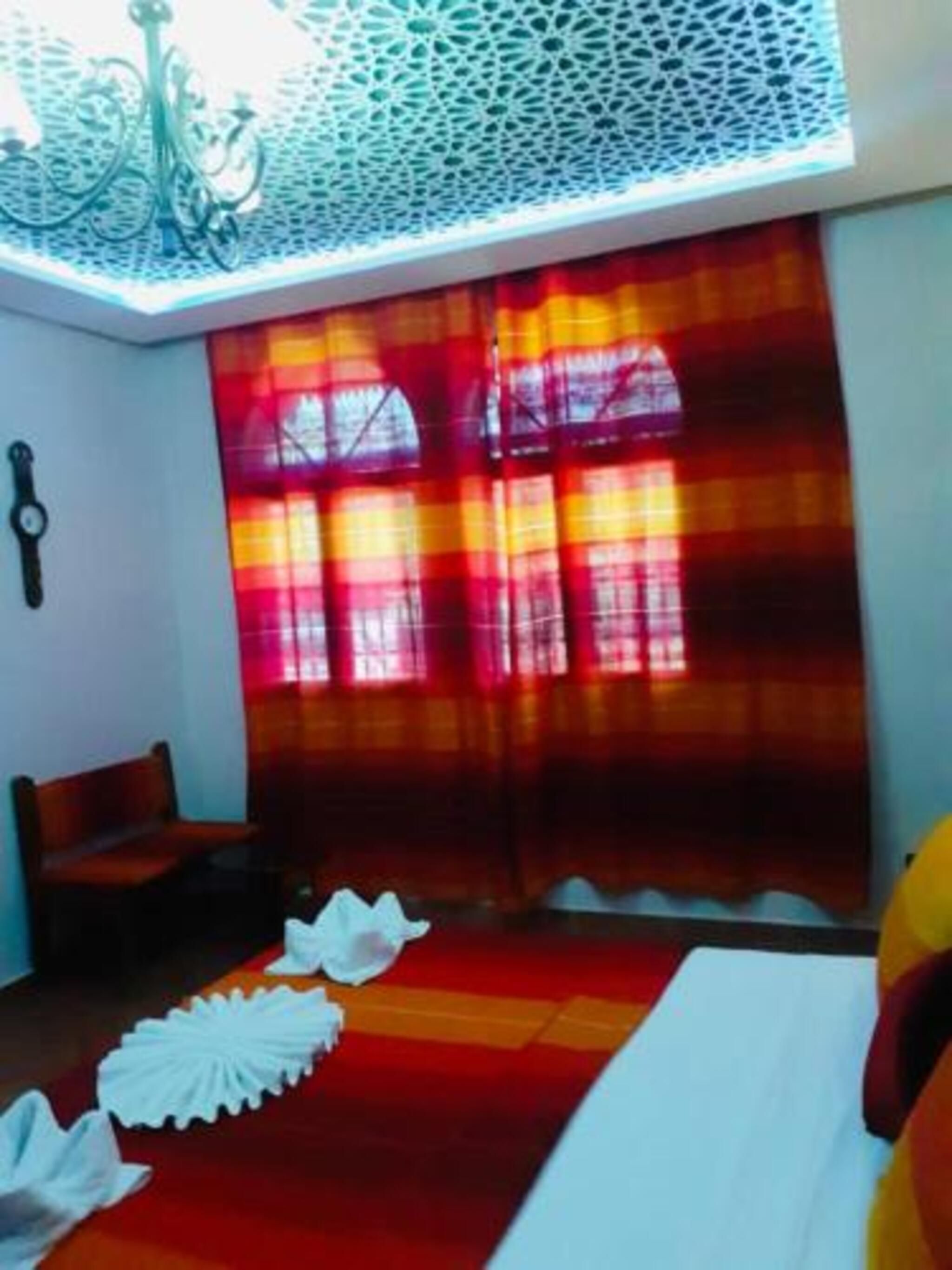 A room with a skylight, a bed, a chair, and a window with curtains.
