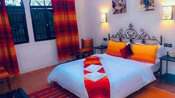 Una cama bien hecha con almohadas, una mesita, una silla y una lámpara de pared.