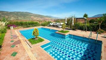 A rectangular pool with a checkered pattern, surrounded by a tiled deck and a small garden area with a tree.