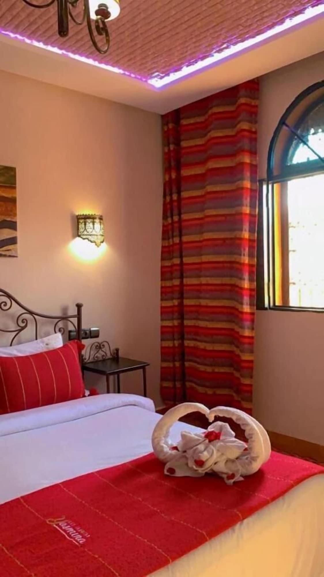 A hotel room with a bed, a wall-mounted light, a window with curtains, and a decorative swan on the bed.