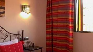 A hotel room with a bed, a wall-mounted light, a window with curtains, and a decorative swan on the bed.
