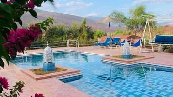 A pool area with lounge chairs and a view of mountains.