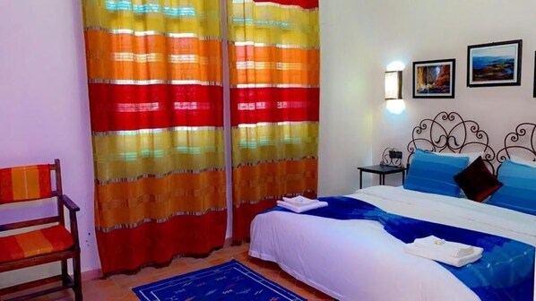 Quarto com cama, cortinas, uma cadeira, mesa de cabeceira e luzes fixadas na parede.