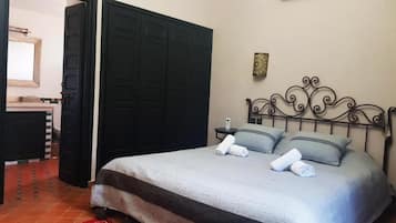 Un dormitorio con cama, una mesita de noche, aire acondicionado instalado en la pared y una puerta que da a otra habitación.