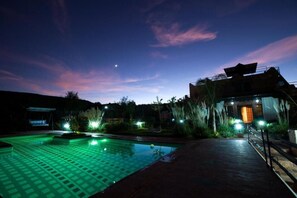 Ein Nachtblick auf einen Hotelpoolbereich mit klarem Himmel, einem Gebäude mit geneigtem Dach und einem gut beleuchteten Weg.