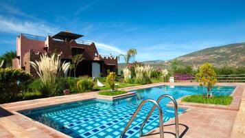 A swimming pool with a geometric tile pattern, surrounded by a landscaped garden with various plants and a view of a mountainous landscape.