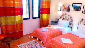 A room with two beds, a small table, and a window with curtains.