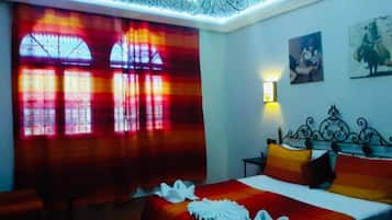 Una habitación de hotel con una cama, un banco, una lámpara de araña y una ventana con cortinas.