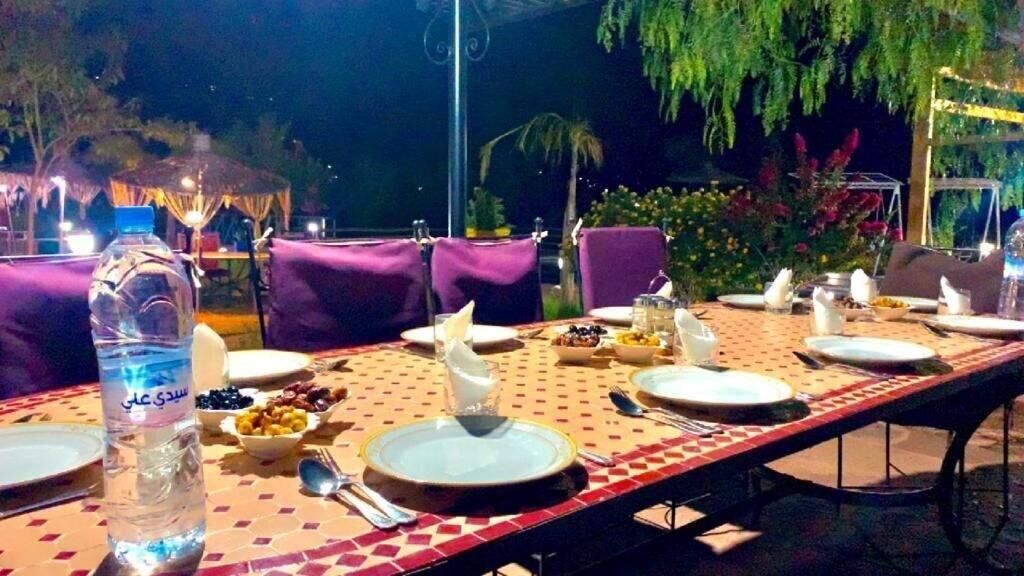 An outdoor dining area with tables set for a meal, surrounded by greenery and evening lighting.