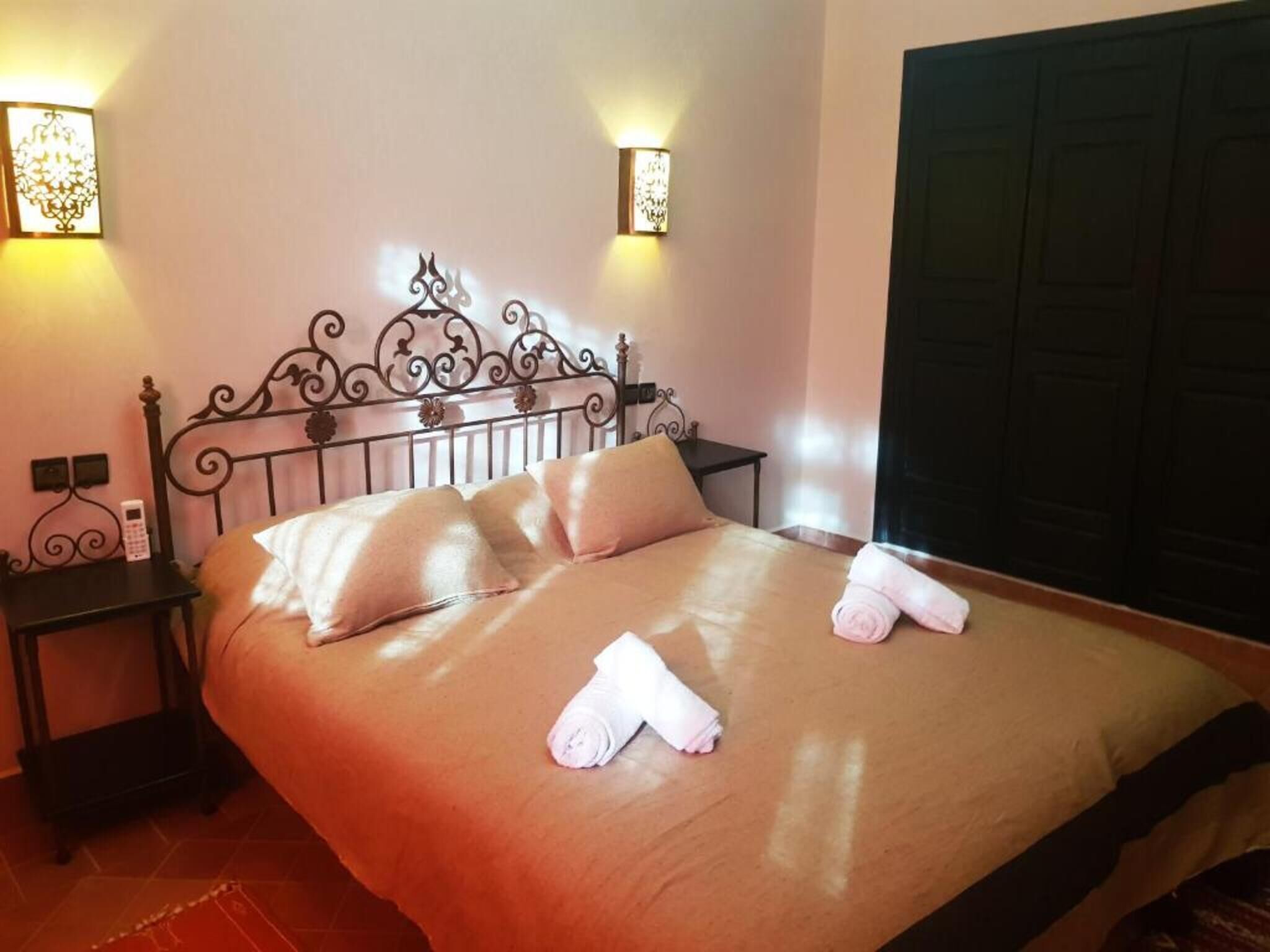 Un lit bien fait, avec des oreillers et des serviettes, une table de chevet avec un téléphone et des lampes fixées au mur.
