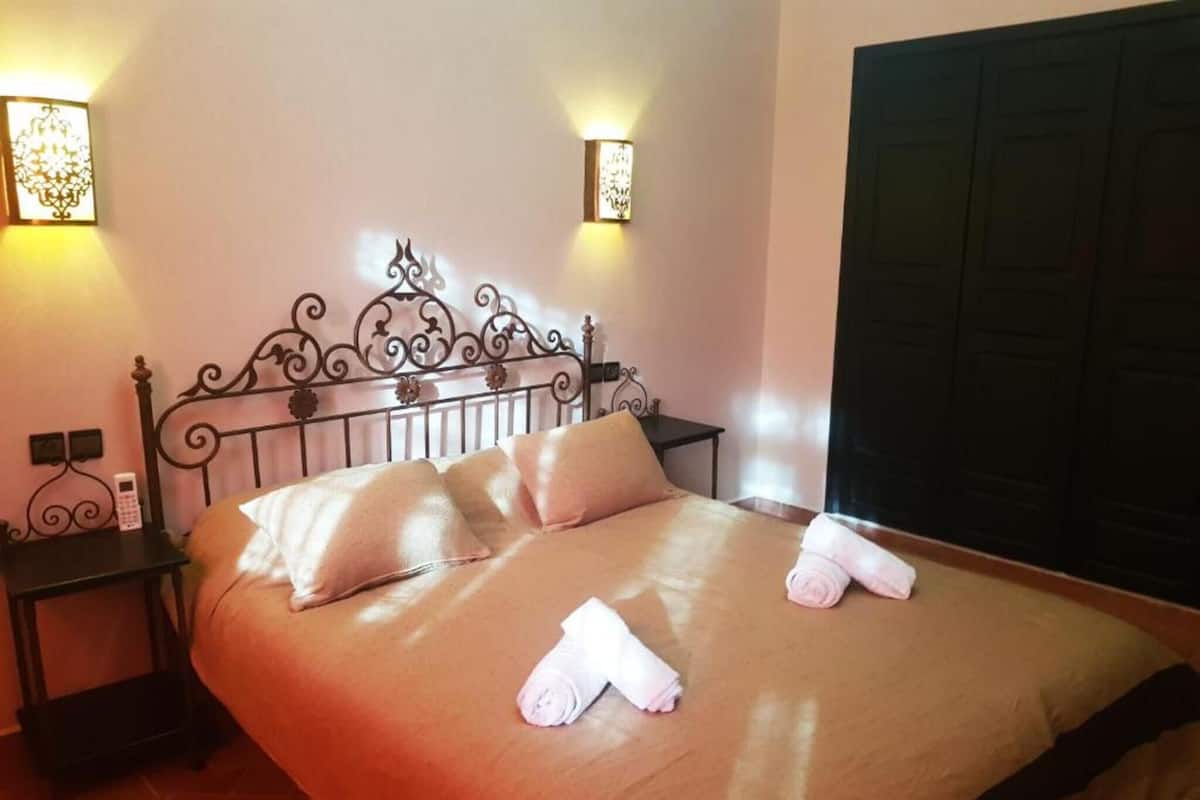 A neatly made bed with pillows and towels, a bedside table with a phone, and wall-mounted lamps.