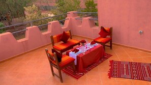 Una terraza con una mesa preparada para dos, dos sillas, un mantel rojo y una alfombra estampada.