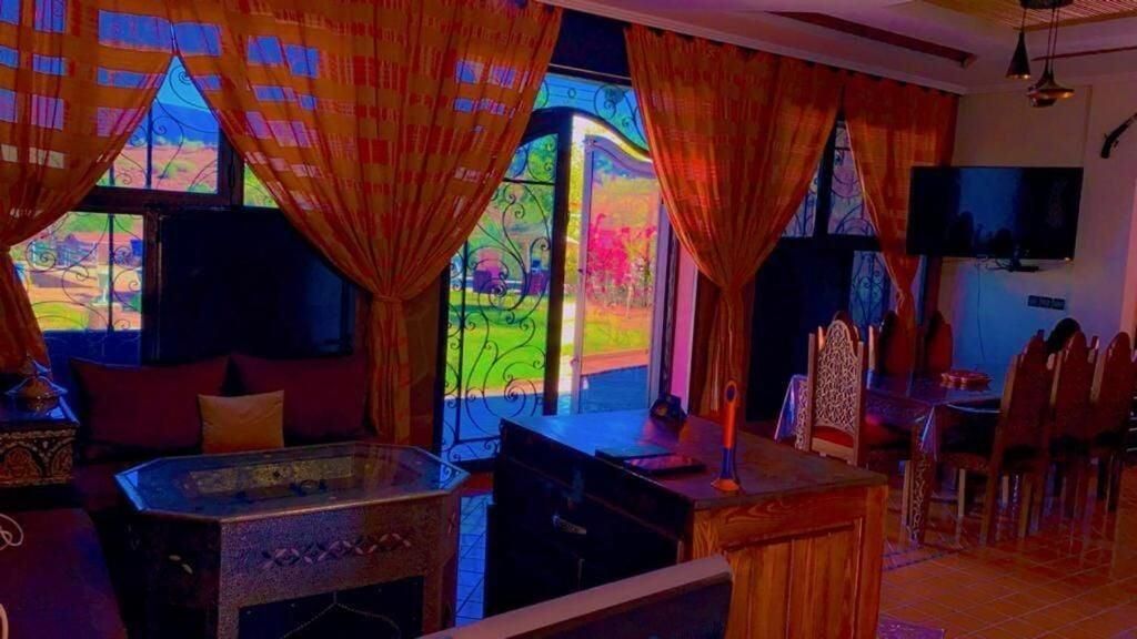 A room with a glass table, curtains, a TV, and a view of greenery outside.