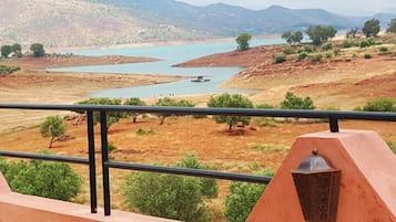 A balcony with a metal railing overlooking a landscape with a river and distant mountains.