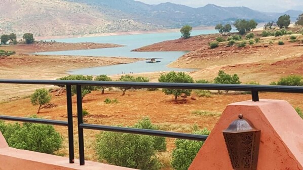 Un balcón con barandilla de metal que da a un paisaje con río y montañas a lo lejos.