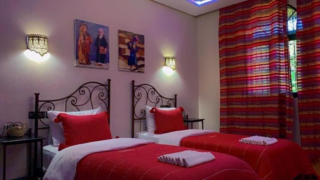 A hotel room with two beds, red bedding, wall-mounted light fixtures, and artwork.