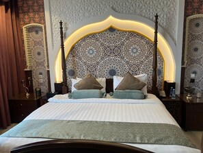 A hotel room with a large bed, ornate headboard, and patterned wall decor. - Holiday Villahail (Ha'il)