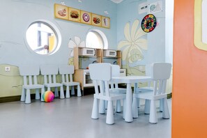 A children's playroom with white chairs, a colorful ball, and wall decorations including food illustrations and a dartboard. - Aluasun Helios Beach (Nessebar)