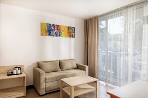 A modern living room with a sofa, a coffee table, a side table, and a large window with sheer curtains. - Aluasun Helios Beach (Nessebar)