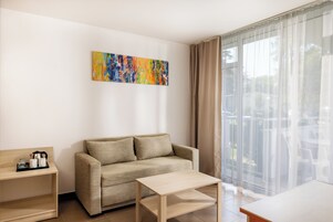 Una sala de estar moderna con un sofá, una mesa de centro, una mesita auxiliar y un gran ventanal con cortinas translúcidas.