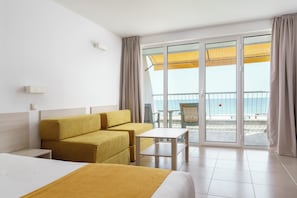 A hotel room with a bed, a sofa, a small table, and a balcony with a view of the sea.