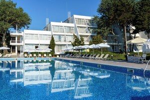 Una piscina con sillones de playa y sombrillas, rodeada de edificios modernos con balcones.