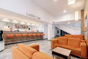 A lobby with orange seating, a bar area, and a staircase.