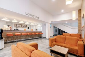 En lobby med orange siddemøbler, et barområde og en trappe.
