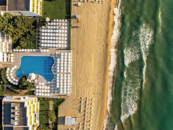 An aerial view of a beach resort with a swimming pool, sun umbrellas, and a sandy beach. - Aluasun Helios Beach (Nessebar)