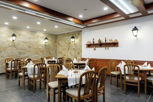 Un restaurante con mesas y sillas de madera, paredes de piedra y lámparas fijadas a la pared.