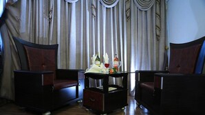 A room with two dark armchairs, a small table with a bottle and glass, and a curtain backdrop.