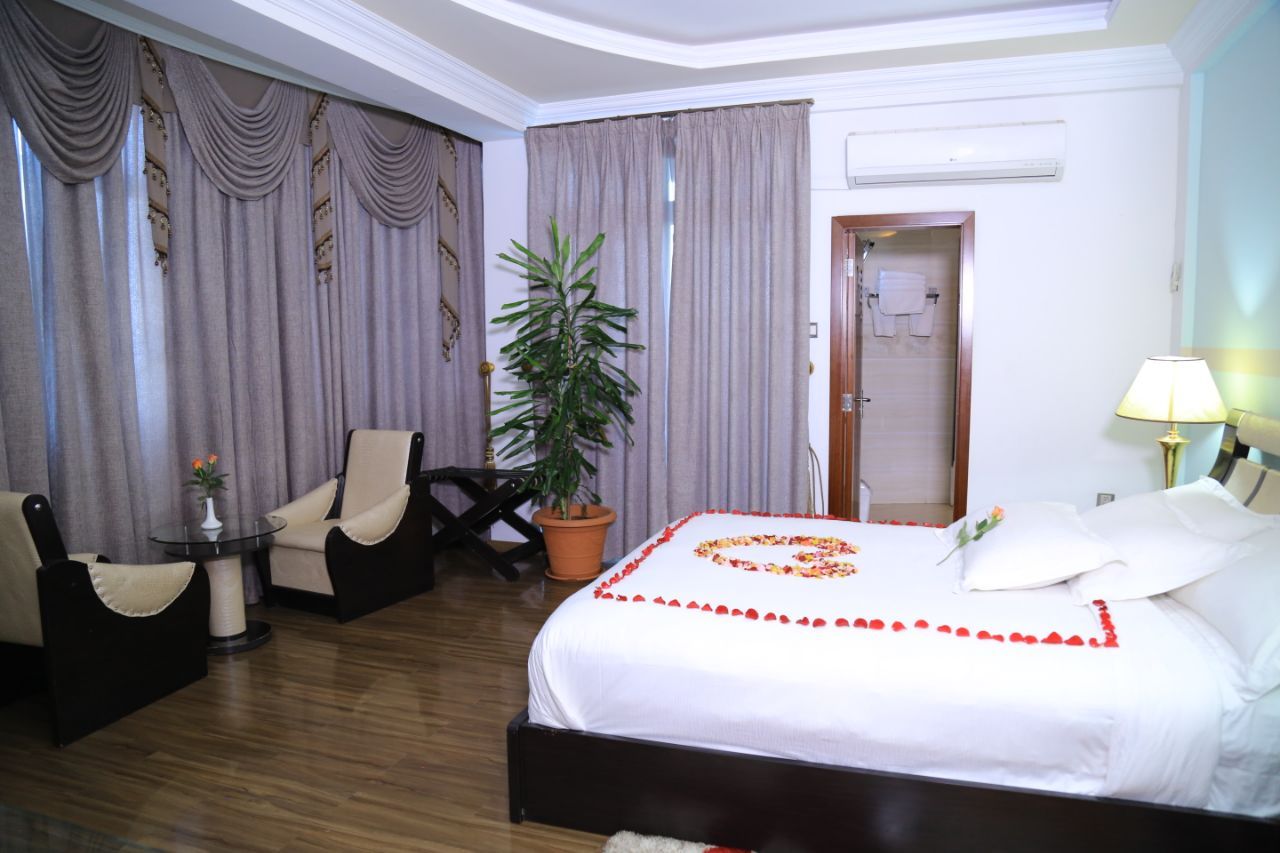 A hotel room with a bed, a chair, a table, a potted plant, and a door leading to a bathroom.