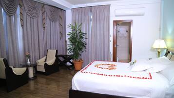 A hotel room with a bed, a chair, a table, a potted plant, and a door leading to a bathroom.