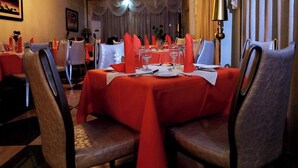 A dining area with tables set for four, each with a red tablecloth, white napkins, and silverware.