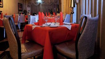 A dining area with tables set for four, each with a red tablecloth, white napkins, and silverware.