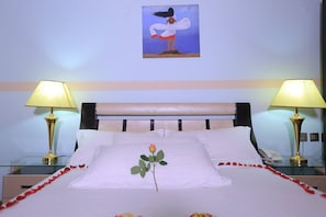 A hotel room with a bed, two bedside lamps, a painting on the wall, and a single rose on the pillow. - Ker Awud International Hotel (Awassa)