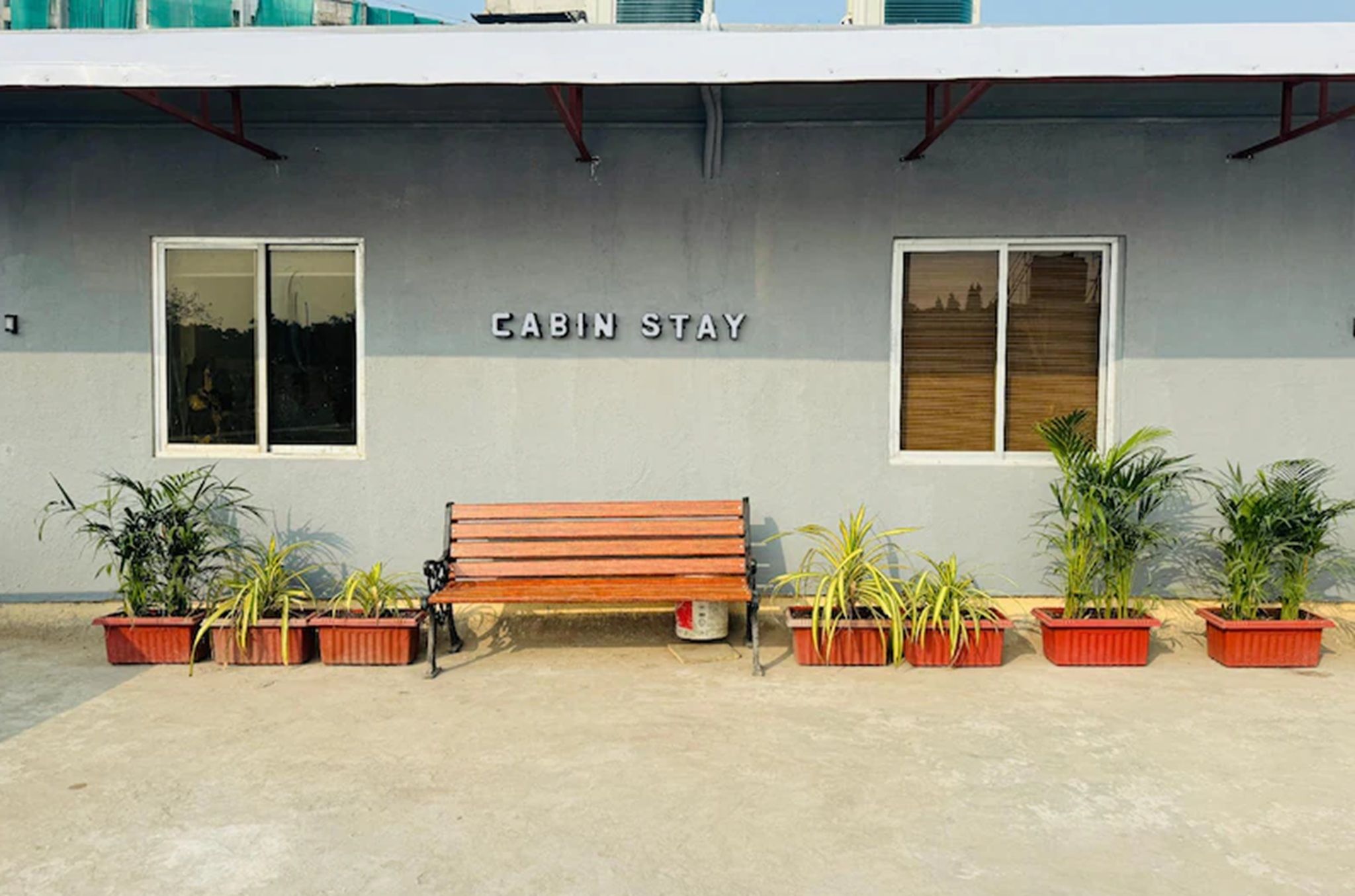 A building labeled 'CABIN STAY' with a wooden bench and potted plants in front.